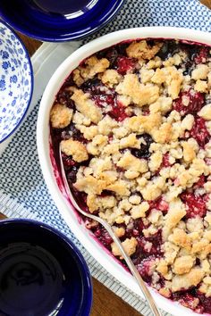 a blueberry cobbler in a white bowl on a table with plates and bowls