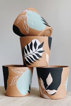 four planters with leaves painted on them are sitting on a table and one is empty