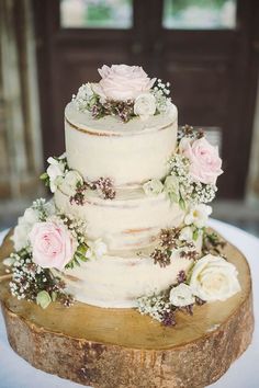 a white wedding cake with pink flowers and greenery on top sits on a wooden slice