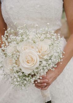 a bride holding a bouquet of white roses and baby's breath in her hand