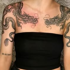 a woman with dragon tattoos on her chest and arm is standing in front of a wall