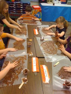 several children are sitting at a table making brownies with plastic wrappers on them