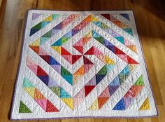 a multicolored quilt is laying on the floor in front of a wooden table