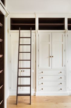 a ladder leaning against the wall in a room with white cupboards and drawers on either side