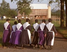 five women in purple and white robes walking down a road with a barn in the background