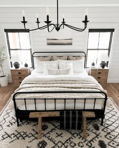 a bedroom with white walls, black and white bedding, wooden flooring and chandelier