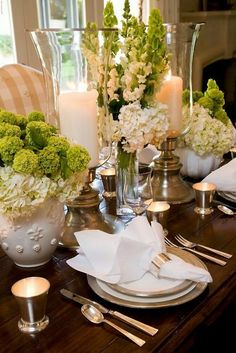 the table is set with white and green flowers in vases, silverware, and candles