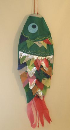 a paper fish hanging on the wall next to a white wall with red and green streamers