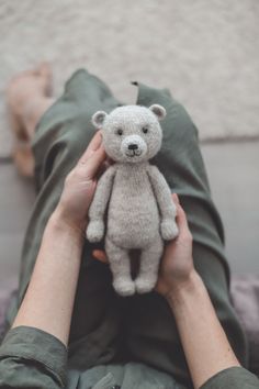 a person holding a small teddy bear in their hands while laying on a bed with green sheets