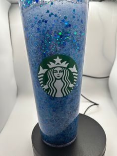 a starbucks cup with blue glitter on it sitting on top of a black stand in front of a white wall