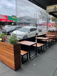 several wooden benches sitting on the side of a road next to a building with cars parked in front of it