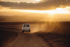 a white van driving down a dirt road in the middle of an open field at sunset