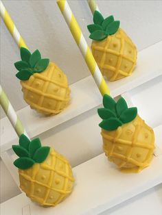 four pineapples with green leaves and yellow straws on them sitting on white shelves