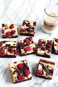 desserts with raspberries and chocolate are arranged on a marble table next to a glass of milk