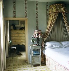 a bed sitting next to a dresser with a lamp on top of it