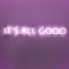 the words it's all good are lit up against a purple wall in an empty room