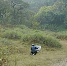 a man sitting on a bench in the middle of a field with trees and bushes