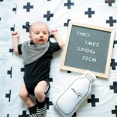 a baby laying on a bed next to a chalkboard with the names of two times