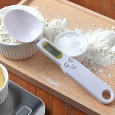 an electronic scale and measuring cup on a wooden table with flour in the bowl next to it