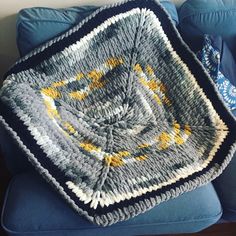 a crocheted blanket sitting on top of a blue couch next to a pillow