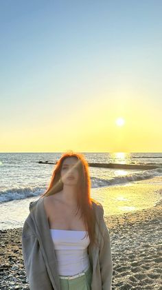 a woman standing on top of a sandy beach next to the ocean with her hair blowing in the wind