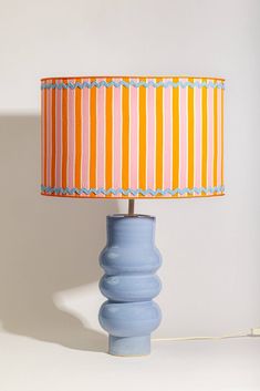 a blue table lamp with an orange and white striped shade on the top, against a white wall