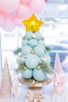 a christmas tree made out of balloons on a table with other decorations and trees in the background