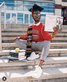 a young man sitting on steps holding a book and wearing a graduation cap with his hands in the air