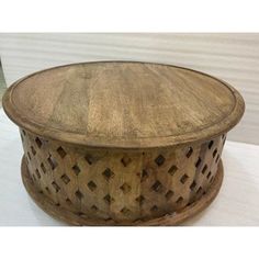 a round wooden table sitting on top of a white floor next to a wall and window