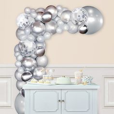 a table topped with silver balloons on top of a wall next to a white cabinet