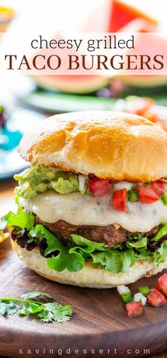 a cheeseburger with lettuce, tomatoes and other toppings on a cutting board