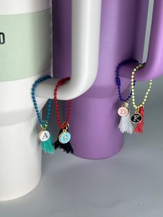 three necklaces hanging from the side of a purple vase next to two other items