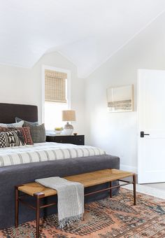 a bed sitting on top of a rug next to a wooden footstool in a bedroom