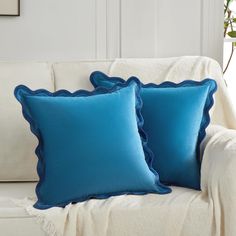 two blue pillows sitting on top of a white couch