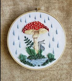 a mushroom with a red hat is in the rain embroideryed on a white hoop