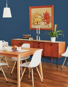 a dining room with blue walls and wooden floors, white chairs and a wood table