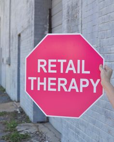 a person holding up a red stop sign that says retail therapy on the side of a building