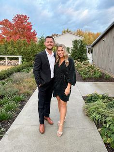 a man and woman are standing on a walkway in front of a house with colorful trees