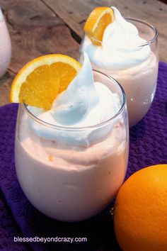 two glasses filled with oranges and whipped cream next to an orange on a purple towel