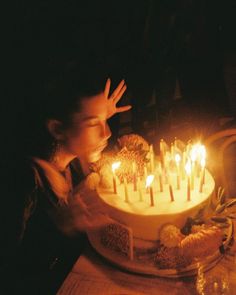 a woman blowing out candles on a cake with her hands in front of the cake