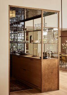 a kitchen with wooden cabinets and glass shelves on the wall, in front of a dining room table