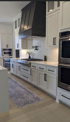 a kitchen with white cabinets and stainless steel ovens, stove top hood, and rug