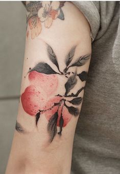 a woman's arm with an apple and leaves tattoo on her left arm is shown