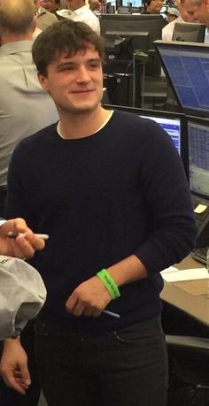 a man standing in front of two computer desks with people working on computers behind him