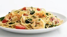 pasta with shrimp, tomatoes and spinach in a white bowl on a white table