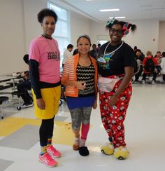 three women standing next to each other in front of a room full of people wearing colorful clothing