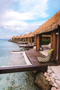 a dock with chairs and thatched huts on the water