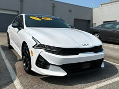 a white car parked in a parking lot with two black cars behind it and yellow stickers on the hood