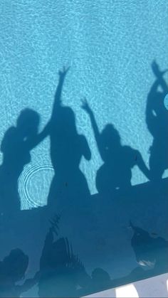 the shadow of two people standing in front of a swimming pool with their hands up