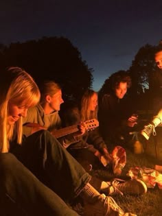 a group of young people sitting around a campfire playing guitars and drinking beer at night